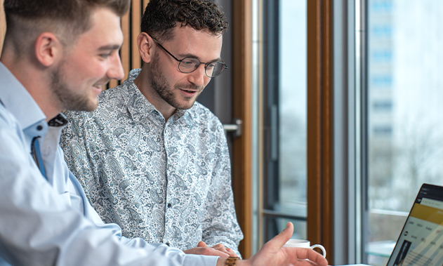 Zwei Personen schauen auf einen Laptop und lächeln.